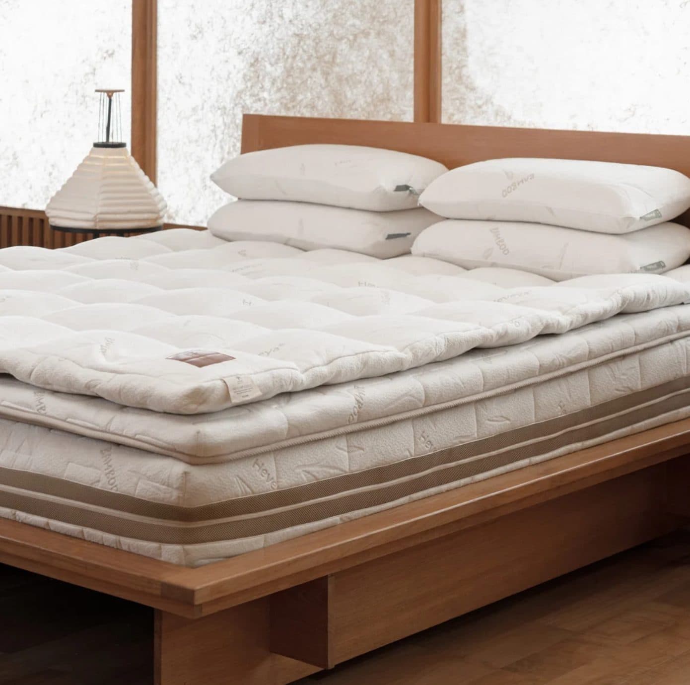 A Heveya mattress on a wooden bed frame, dressed with a quilted topper and four Heveya pillows.